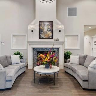 A modern living room featuring a fireplace, curved sofas, and a centerpiece coffee table adorned with flowers.