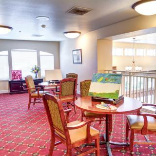 A cozy lounge area with tables and chairs, carpeted flooring, and ample natural light from large windows.