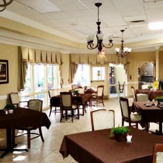 A well-decorated dining room with several tables and chairs, featuring elegant chandeliers and large windows with curtains.