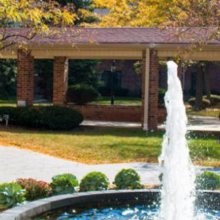 A fountain surrounded by autumn trees and a brick walkway.