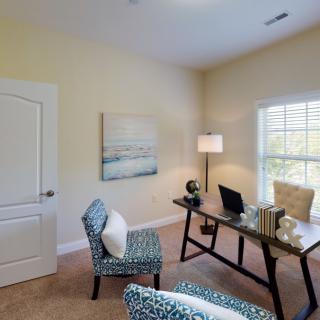 A cozy home office setup with a desk, chairs, and a bright window.