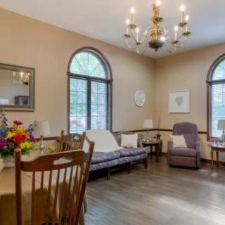 A cozy living room featuring a dining table with flowers, comfortable seating, and large arched windows.