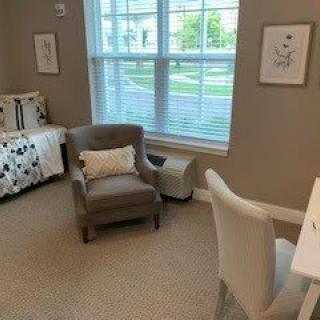 A cozy bedroom with a comfortable chair, small desk, and large window letting in natural light.