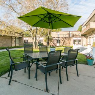 Outdoor patio setup with a green umbrella, table, and chairs in a garden setting.