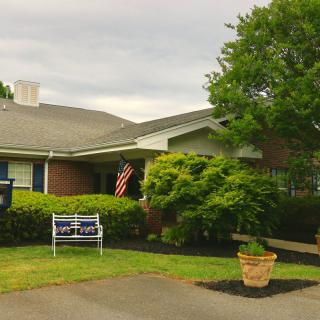 A quaint residential house with a garden, displaying an American flag and a bench on the front lawn.