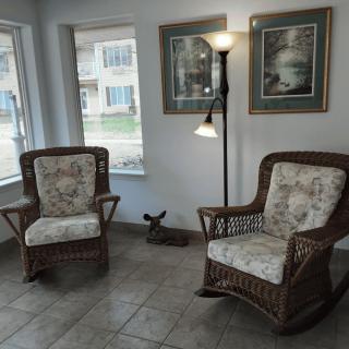 A cozy living room corner with two wicker chairs, a standing lamp, and wall art.