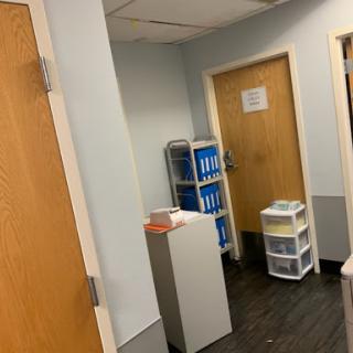 A view of an office hallway featuring doors, storage units, and filing cabinets.