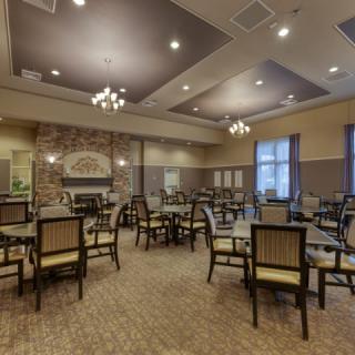 A spacious and elegantly designed dining room with multiple tables and chairs, featuring a brick fireplace and chandeliers.
