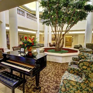 A luxurious lobby with a grand piano, surrounded by comfortable seating and a central plant display.