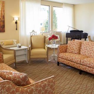 A cozy living room with armchairs, a floral sofa, and a piano by the window.