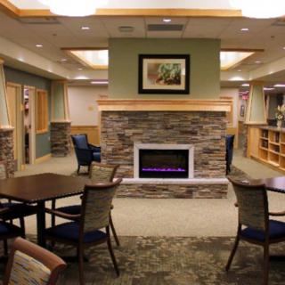 A cozy library interior with a central fireplace, surrounded by tables and chairs.
