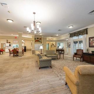 A spacious and well-lit living room area with comfortable seating, a chandelier, and carpeted flooring.