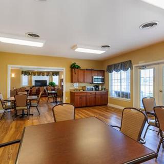 A spacious dining and kitchen area with wooden floors, tables, chairs, and large windows letting in natural light.