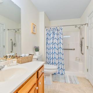 A clean and bright bathroom featuring a shower with a patterned curtain, a sink with a mirror, and neatly organized toiletries.