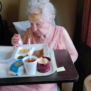 An elderly woman enjoying her meal in a hospital setting.