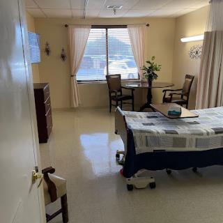 A clean and well-organized hospital patient room with a view, featuring a bed, table, and chairs.