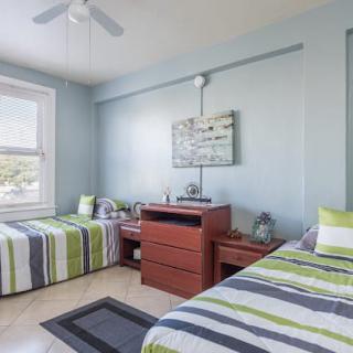 A modern bedroom featuring two twin beds with striped bedding and a central dresser, complete with wall artwork and natural light from a large window.
