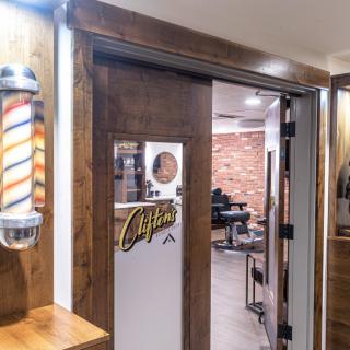 The entrance to a barbershop featuring a traditional barber pole and a view of the interior with exposed brick walls and salon chairs.