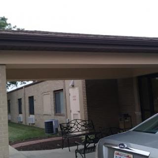 A view of a building with a carport and a parked car in front.