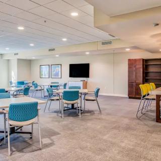 A modern conference room featuring tables and chairs, a television screen, and carpet flooring.