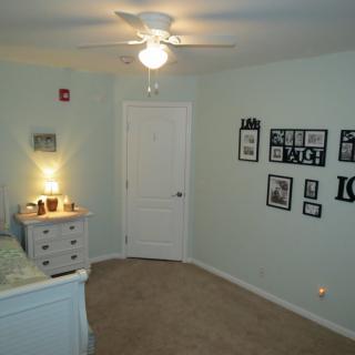 A cozy bedroom featuring a dresser with a lamp, wall art, and a ceiling fan.