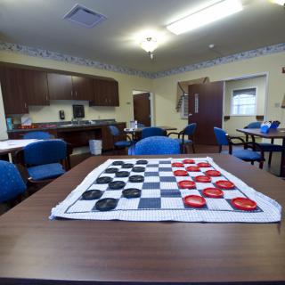 A community game room featuring a checkerboard set up on a table, surrounded by blue chairs.