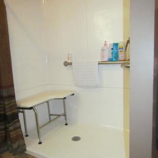 An accessible shower featuring a built-in bench and toiletries on a wall shelf.
