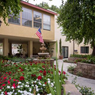 A well-maintained courtyard with colorful flowers and an American flag outside a building.
