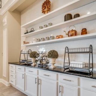 A beautifully organized kitchen with white cabinets, decorated shelves, and a black countertop displaying various kitchenware items.