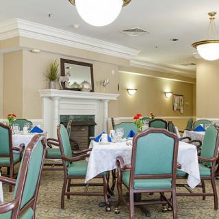 A well-decorated dining room with elegantly set tables and chairs, featuring a cozy fireplace.