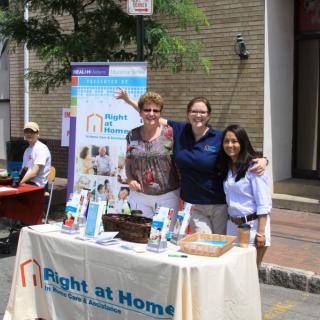 A group of people stand at an information booth for 'Right at Home' during a community event.