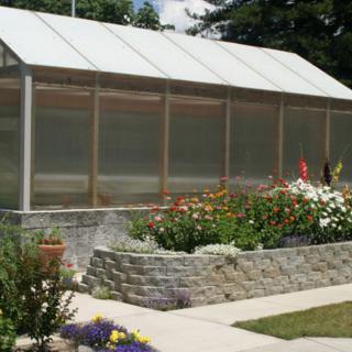 A greenhouse surrounded by a lush garden with colorful flowers.