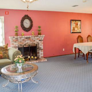 A cozy living room with a brick fireplace, adorned with decorative items and artwork on a red wall, featuring a comfortable seating area and dining space.