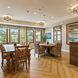 A well-lit dining area with wooden flooring, featuring tables and chairs next to large windows.