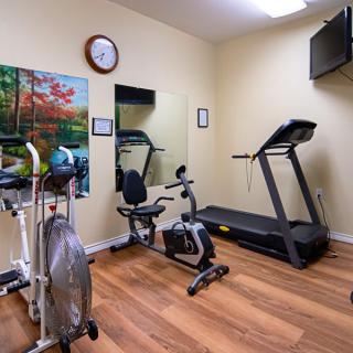 A compact home gym featuring a treadmill, stationary bike, and elliptical machine on wooden floors.