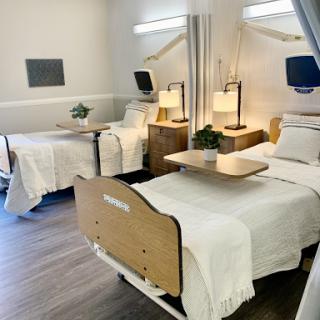 A modern hospital patient room featuring twin beds, bedside tables, and a warm ambiance.