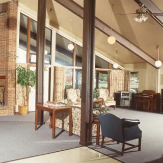 A modern living room with large windows, showcasing wooden beams and a mix of comfortable furniture.