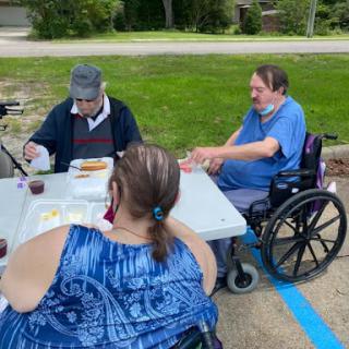 A group of individuals enjoying a meal outdoors, with some participants in wheelchairs.