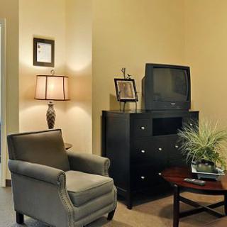 A cozy living room corner with a comfortable chair, an old television on a dresser, and a stylish lamp providing warm lighting.