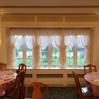 A cozy dining room with elegantly draped windows and neatly arranged tables and chairs.