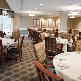 A neatly arranged dining area with round tables and cushioned chairs, ready for guests.