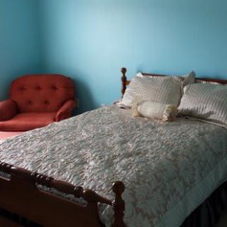 A cozy bedroom with a wooden bed frame, quilted bedding, and a red armchair against blue walls.