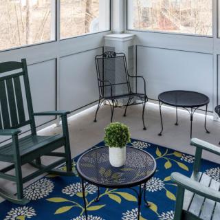 A cozy screened porch with rocking chairs, a small table adorned with a potted plant, and a colorful rug.
