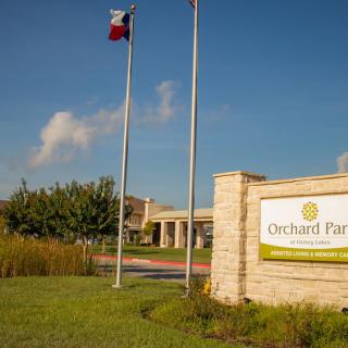 The entrance to Orchard Park, featuring a prominent sign and flagpoles against a blue sky.