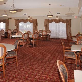 An empty dining room with arranged tables and chairs, featuring a patterned carpet and elegant curtains.