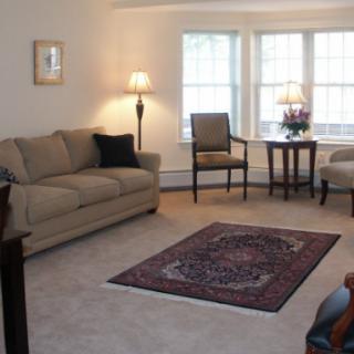 A cozy living room with a sofa, chair, coffee table, and a rug in front of large windows.