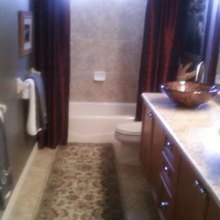 A modern bathroom with a vessel sink, dark curtains, and a patterned rug.