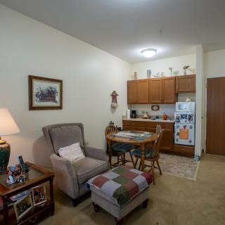 A cozy apartment featuring a small living room area with a comfortable chair and footrest, adjacent to a compact kitchen.