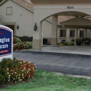 Exterior view of a nursing home with a prominent sign and landscaped entrance.