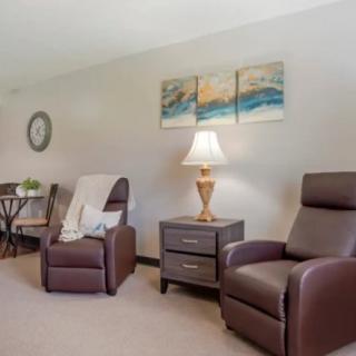 A cozy living room with brown armchairs, a side table with a lamp, and wall art.